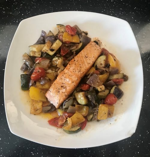 A photo of Salmon and roasted vegetables on a white square plate on a charcoal coloured granite worktop