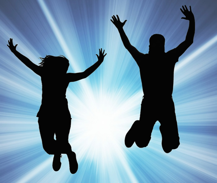 silhouette of man and woman jumping for joy with a bright light shining behind them